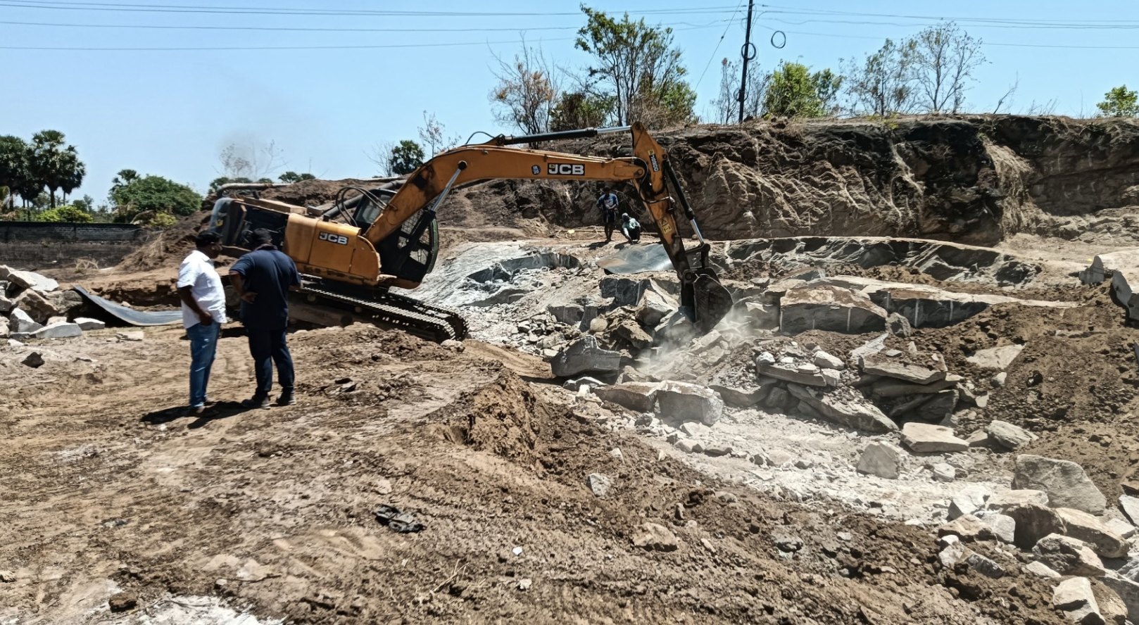 Excavator and workers at the Walayar project site, working around exposed rock